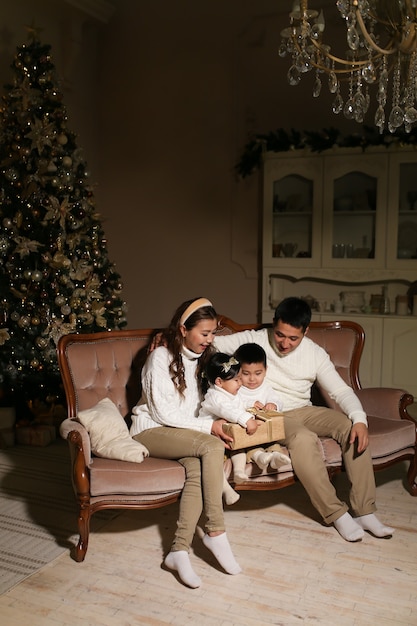 Famiglia asiatica con due bambini apre doni mentre è seduto sul divano vicino all'albero di notte a casa