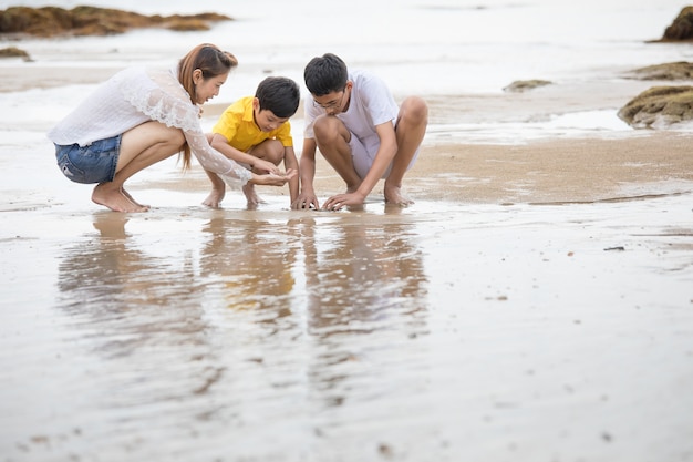 Famiglia asiatica di tre persone in vacanza, madre e figli, che giocano sulla spiaggia tropicale con felicità e divertimento