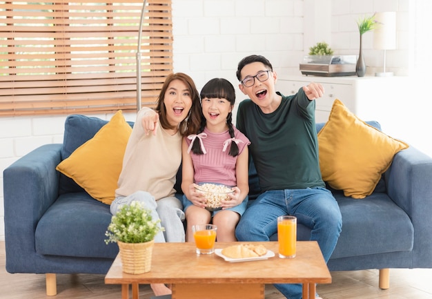 Famiglia asiatica felice che mangia popcorn e guardare la tv insieme sul divano di casa soggiorno. concetto di tempo libero e persone