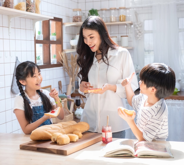 Famiglia asiatica felice in cucina. madre, figlio e figlia diffondono l'igname di fragole sul pane