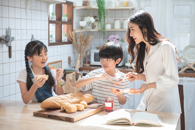 Famiglia asiatica felice in cucina. madre, figlio, figlia e figli diffondono l'igname di fragole sul pane, attività ricreative a casa.