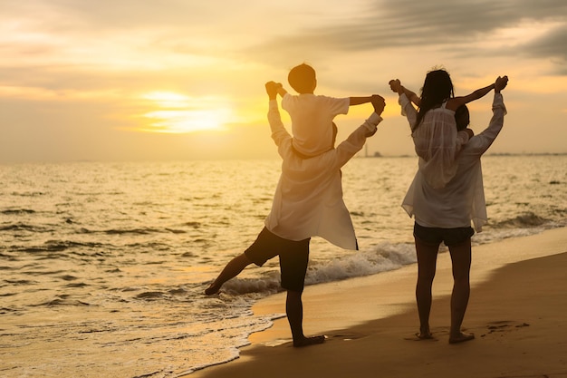 Famiglia asiatica felice sulla spiaggia in vacanza della famiglia che si tiene per mano Figlio e figlia a cavallo dei genitori Si stanno divertendo giocando godendosi il tramonto sulla spiaggia Estate Famiglia e stile di vita