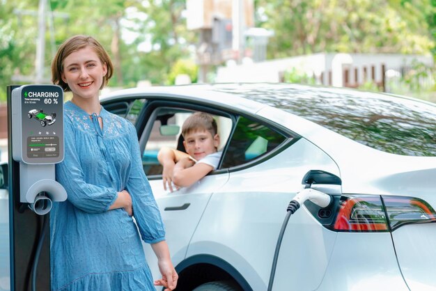 Famiglia attenta all'ambiente con un'auto elettrica ecologica che ricarica la batteria da casa Stazione di ricarica per veicoli elettrici con bambino all'interno dell'auto Tecnologia per auto elettriche e ricaricabili Perpetuo