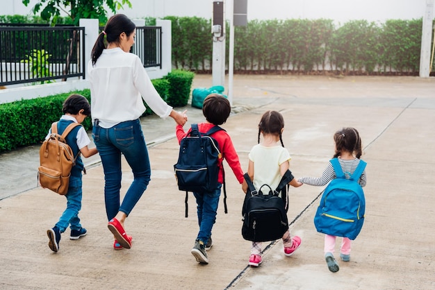 Famiglia bambini bambino figlio ragazza e ragazzo asilo che cammina andando a scuola tenendosi per mano con madre mamma
