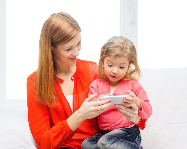 famiglia, bambini, genitorialità, tecnologia e concetto di internet - madre e figlia felici con lo smartphone a casa