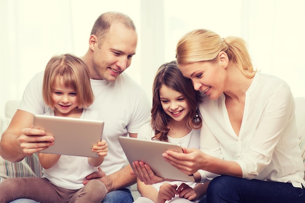 famiglia, bambini, tecnologia, denaro e concetto di casa - famiglia sorridente e due bambine con computer tablet pc a casa