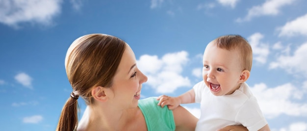 famiglia, bambino e genitorialità concetto - felice sorridente giovane madre con piccolo bambino sopra cielo blu e nuvole sullo sfondo