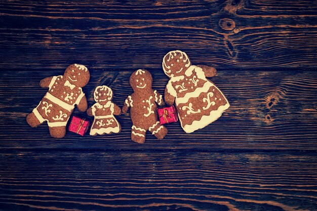 Famiglia carina di panpepato fatto in casa con piccoli regali rossi su fondo di legno scuro. Mockup per offerte stagionali e cartolina delle vacanze