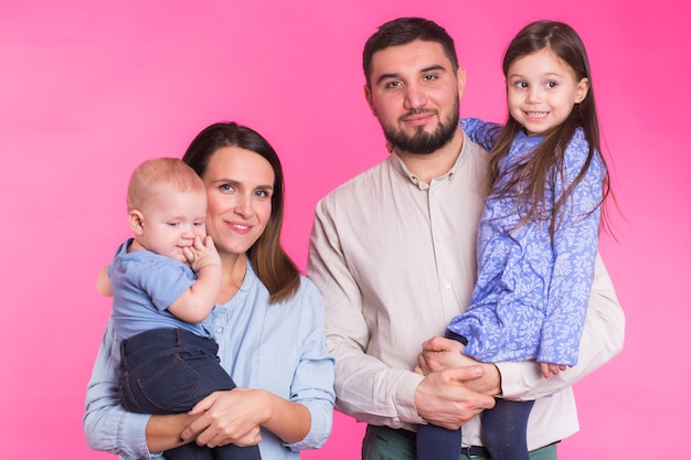 Famiglia carina in posa e sorridente insieme sulla parete rosa.