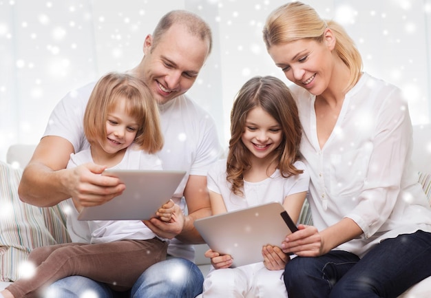 famiglia, casa, tecnologia e persone - madre, padre e bambine sorridenti con computer tablet pc su sfondo di fiocchi di neve