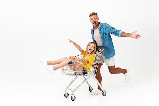 Famiglia caucasica padre e figlia che si divertono mentre fanno un giro nel carrello della spesa isolato su bianco