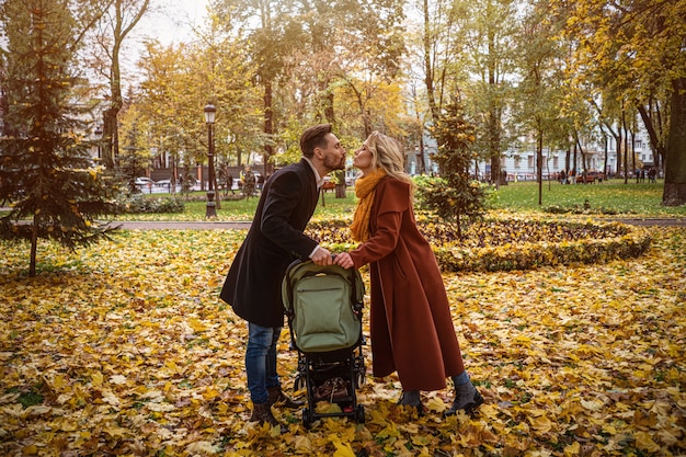 Famiglia che cammina in un parco in autunno con un neonato in un passeggino. Famiglia all'aperto in un golden