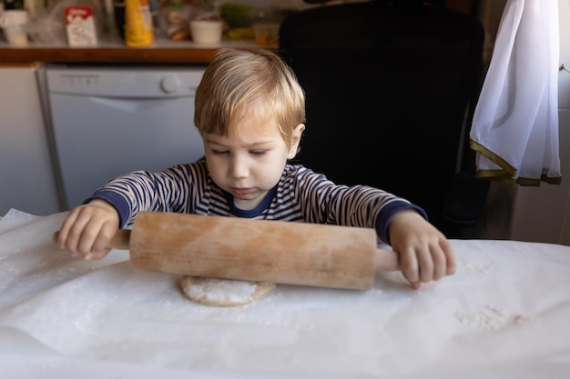 Famiglia che cucina un ragazzino lavora con un mattarello con pasta cruda