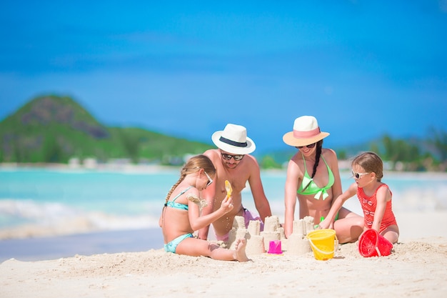 Famiglia che fa il castello della sabbia alla spiaggia bianca tropicale