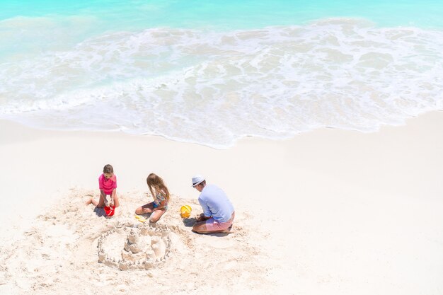 Famiglia che fa il castello di sabbia alla spiaggia bianca tropicale. Vista dall&#39;alto