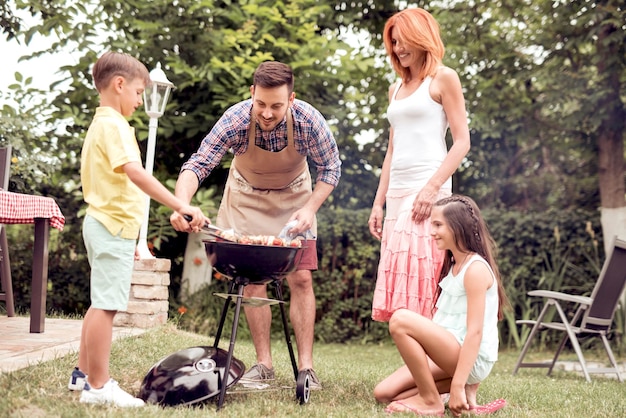 Famiglia che fa una festa barbecue intorno alla griglia