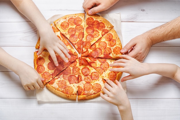 Famiglia che mangia la pizza di peperoni. Bambini e padri con una fetta di pizza.