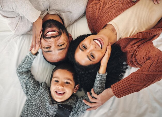 Famiglia che ride e ritratto vista dall'alto sul letto in camera da letto legame e cura in casa Sorriso d'amore e madre felice padre comico e bambino divertente che giocano divertendosi e godendosi il tempo di scherzare insieme