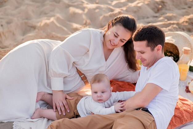 Famiglia che riposa su un picnic sulla spiaggia vicino al mare oceano madre e padre stanno tenendo un bambino una famiglia felice