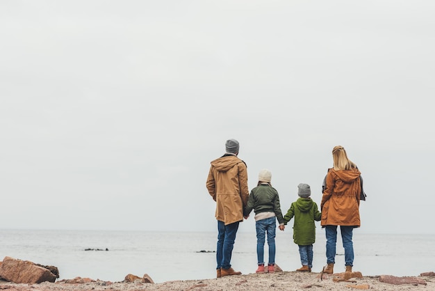 famiglia che si tiene per mano e guarda il mare in una nuvolosa giornata autunnale