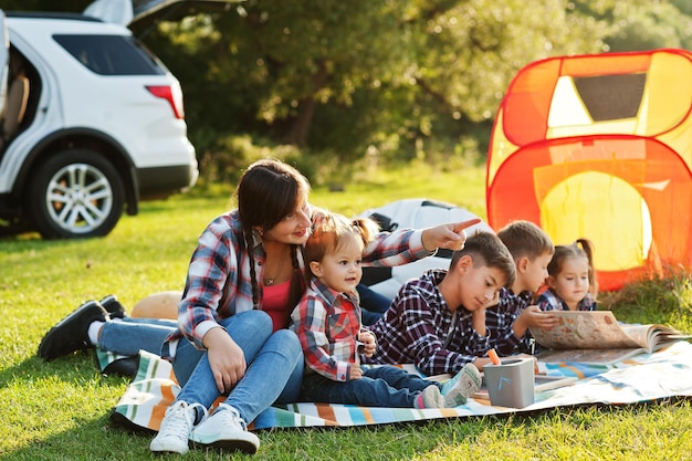 Famiglia che trascorre del tempo insieme Madre con quattro bambini all'aperto in una coperta da picnic contro il loro suv americano