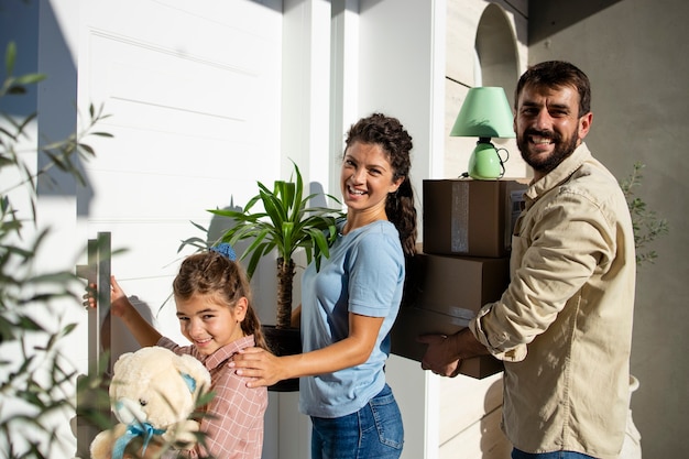 Famiglia che trasporta scatole e fiori mentre entra nella loro nuova casa attraverso la porta d'ingresso