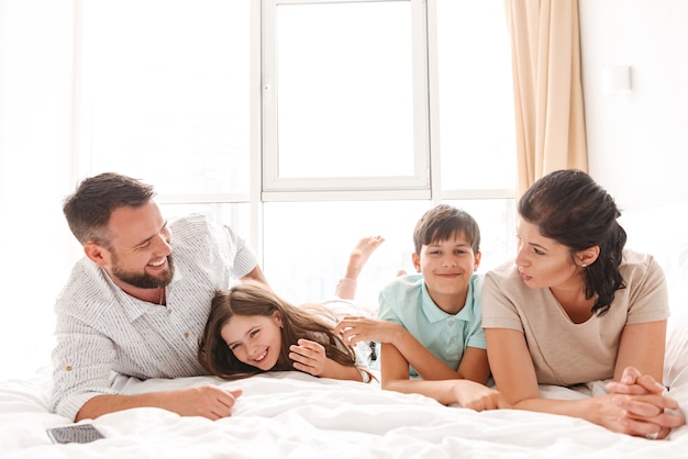 famiglia con due bambini che ridono e sdraiati insieme sul letto in appartamento