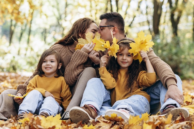 Famiglia con due figlie che si siedono nel parco in foglie di autunno