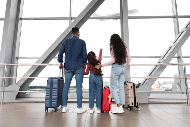 Famiglia con figlia guardando la partenza dell'aereo fuori dalla finestra in aeroporto