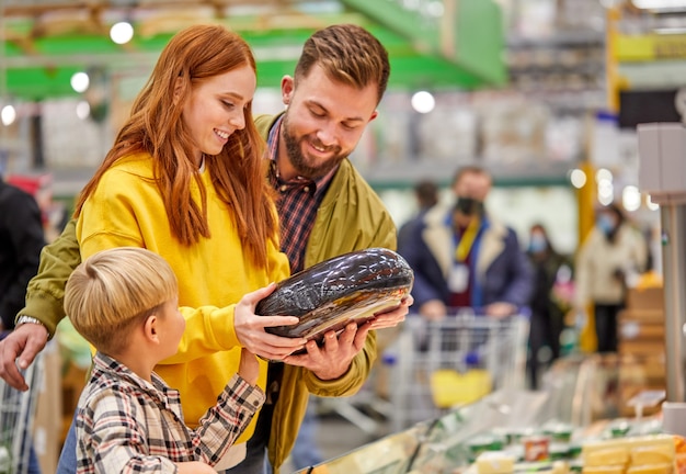 Famiglia con figlio che compra verdura fresca, scegli la migliore, donna discute l'acquisto con il marito