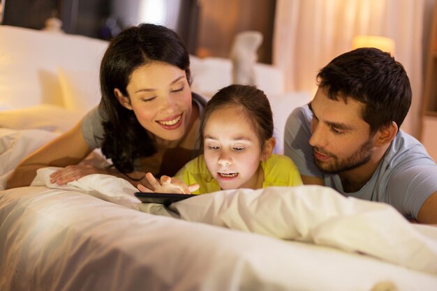 famiglia con tablet sul letto di notte a casa