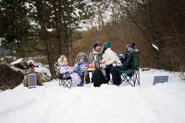 Famiglia con tre bambini nella foresta invernale che trascorrono del tempo insieme durante un picnic