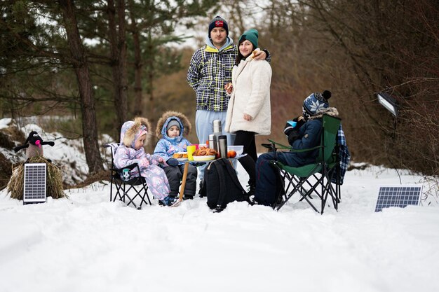 Famiglia con tre bambini nella foresta invernale che trascorrono del tempo insieme durante un picnic