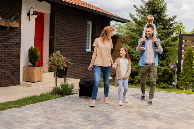 Famiglia con una madre padre figlio e figlia che camminano con i bagagli fuori sul portico anteriore di una casa di mattoni