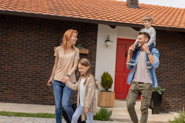 Famiglia con una madre padre figlio e figlia che camminano con i bagagli fuori sul portico anteriore di una casa di mattoni