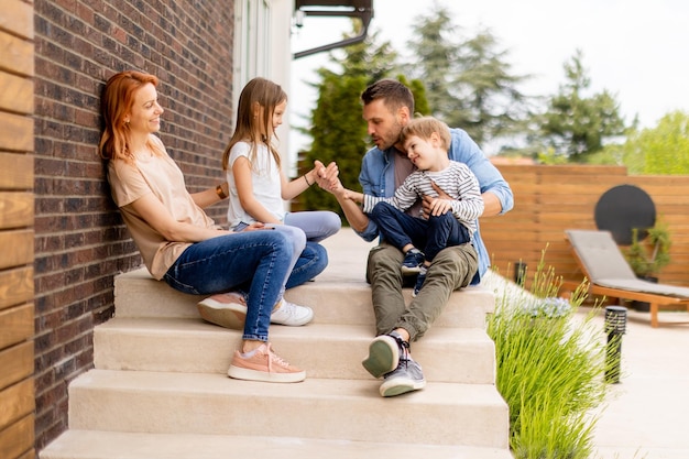 Famiglia con una madre padre figlio e figlia seduti fuori sui gradini di un portico anteriore di una casa di mattoni