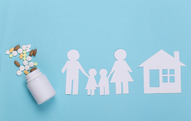 Famiglia di catena di carta con casa, pillole di bottiglia sul blu, concetto di assicurazione sanitaria