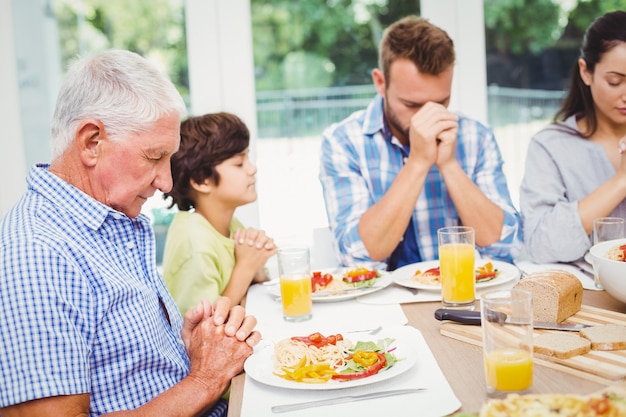 Famiglia di diverse generazioni che prega al tavolo da pranzo