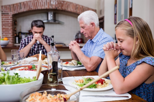 Famiglia di diverse generazioni che prega prima di consumare il pasto