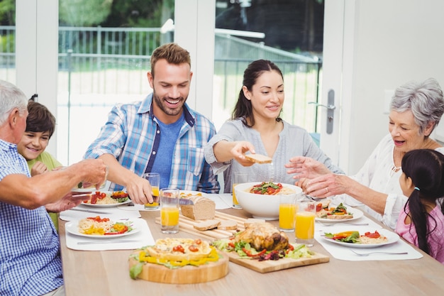 Famiglia di diverse generazioni sorridente che mangia alimento al tavolo da pranzo