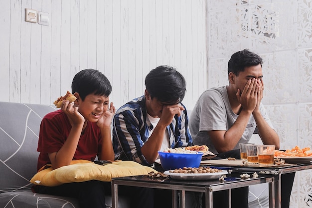 Famiglia di fratelli asiatici seduta sul divano in soggiorno e guardando film spaventosi