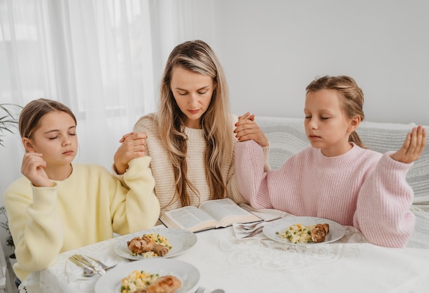 Famiglia di madre e figlie che pregano a tavola