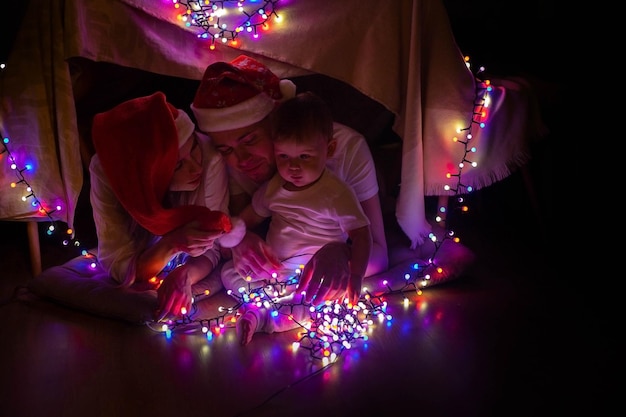 Famiglia di madre, padre e figlio che decorano la tenda dei bambini con le luci di Natale