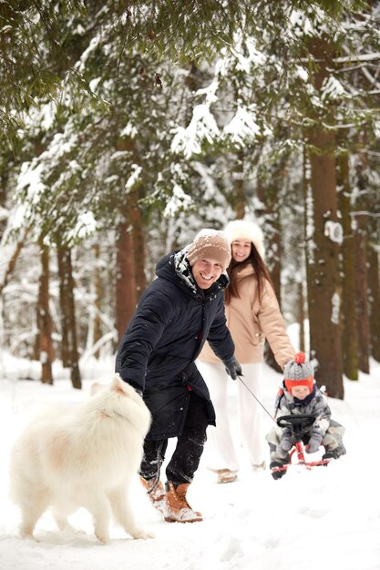 Famiglia di madre padre e figlio che si divertono nel bosco invernale innevato con un cane allegro