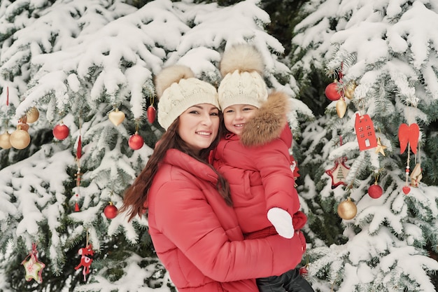 Famiglia di natale nel parco di inverno. La madre felice della famiglia e la figlia del bambino che si divertono, giocando all'inverno camminano all'aperto. Divertimento in famiglia all'aperto in vacanza di Natale. Abbigliamento invernale per neonati e bambini.