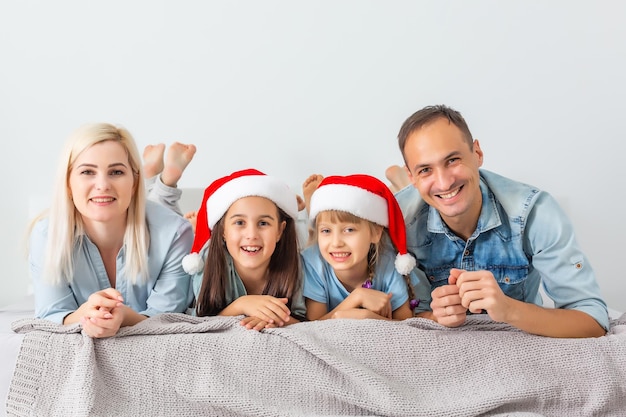 Famiglia di Natale sdraiata a letto bianco con cappelli rossi. Genitori e figlio felici