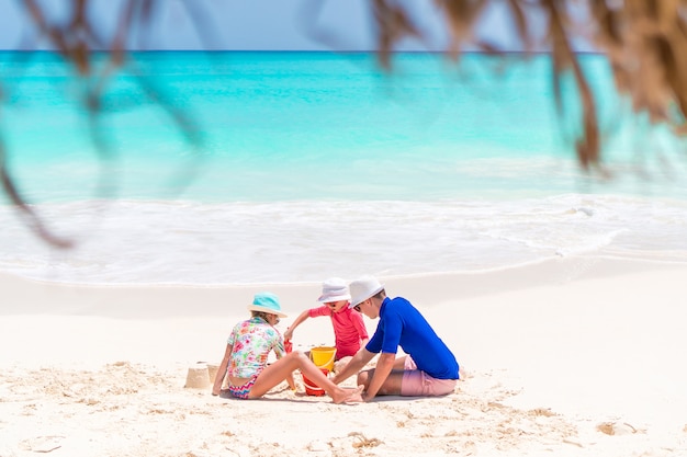 Famiglia di papà e bambini che fanno il castello di sabbia in spiaggia tropicale