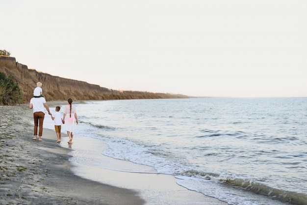 Famiglia di quattro persone che cammina lungo la riva del mare. Genitori e due figli. Vista posteriore