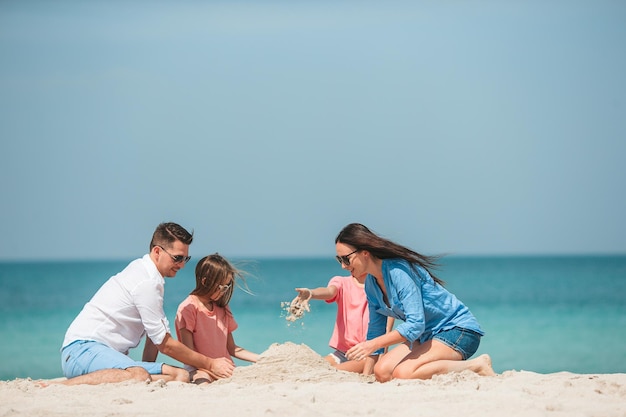 Famiglia di quattro persone che fanno un castello di sabbia sulla spiaggia bianca tropicale