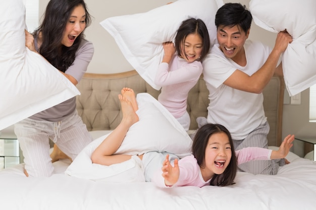 Famiglia di quattro persone che hanno lotta con i cuscini sul letto